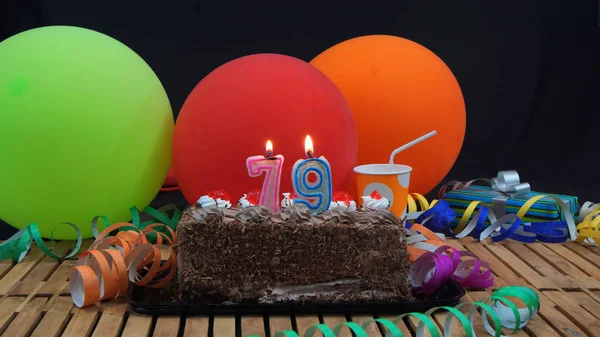 Renkli Balonlar, hediyeler, plastik bardak ve flamalar arka plan siyah arka plan ile rustik ahşap masa üzerinde yanan mumlar ile Çikolatalı doğum günü pastası — Stok fotoğraf