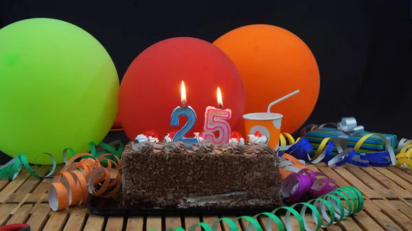 蝋燭が燃えて黒い背景にカラフルな風船、ギフト、プラスチック カップや鯉のぼりの背景の素朴な木製テーブルの上のチョコレートの誕生日ケーキ — ストック写真