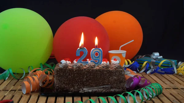 Chocolade verjaardagstaart met kaarsen branden op rustieke houten tafel met achtergrond van kleurrijke ballonnen, geschenken, plastic bekers en wimpels met zwarte achtergrond — Stockfoto