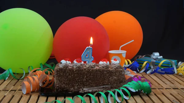 Torta di compleanno al cioccolato con candele che bruciano su un tavolo di legno rustico con sfondo di palloncini colorati, regali, bicchieri di plastica e stelle filanti con sfondo nero — Foto Stock