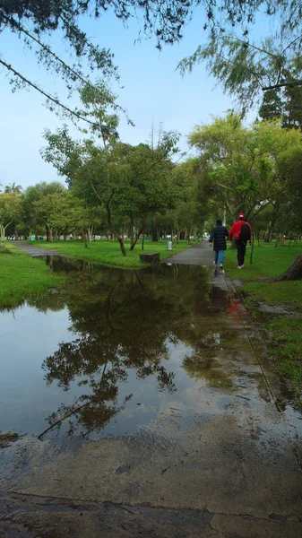 Dois homens caminhando no parque La Carolina ao lado de uma grande poça de água após a chuva. Quito - Equador — Fotografia de Stock