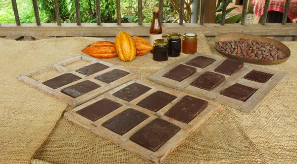 Blocs de chocolat faits à la main à l'intérieur de moules en bois, fruits de cacao mûrs et bocaux en verre avec des produits de cacao sur une table recouverte de jute — Photo