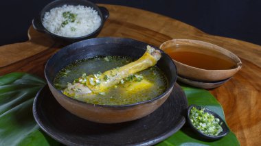 Tavuk çorbası, tipik Ekvador yemeği. Bu çorba tabağın içinde tavuk budu ile birlikte geliyor, yanında beyaz pirinç ve guayusa suyu ile siyah bir arka planda kırsal ahşap bir masa üzerinde.