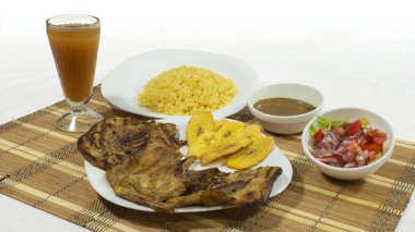 Yanında domuz pirzolası, kızarmış muz, salata ve beyaz zemin üzerinde limonata olan cam bardakla birlikte sarı pirinç.