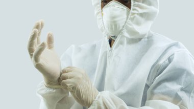 Maskeli ve beyaz bioprotatif giysili doktor beyaz arka plana lateks eldiven takıyor.