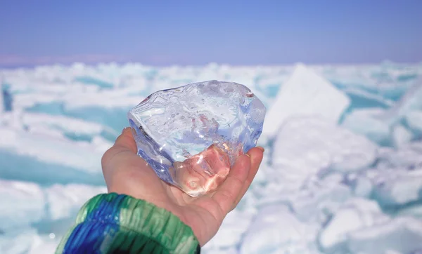 A piece of crystal transparent ice in the hand against frozen lake in sunny day — Stock Photo, Image
