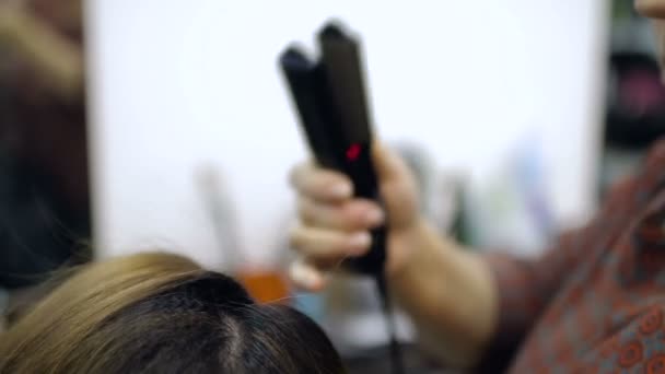Primer plano de un peluquero alisando el cabello largo con planchas para el cabello . — Vídeo de stock