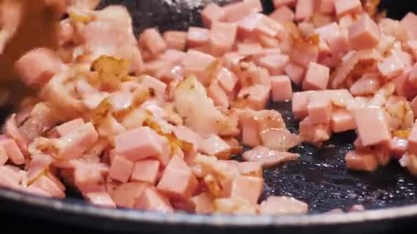 Το ψιλοκομμένο μπέικον και λουκάνικο τηγανίζονται σε καυτό λάδι σε ένα τηγάνι. — Αρχείο Βίντεο