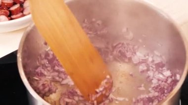 Yağ yavaşça büyük bir tavaya dökülür ince doğranmış kırmızı soğanlar ve ahşap bir spatula ile..