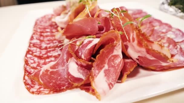En un plato cuadrado blanco, rebanadas cuidadosamente diferentes tipos de carne: salchichas, salami, cervelat y carbonato . — Vídeo de stock