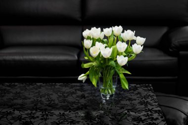 Odadaki cam sehpanın üzerinde siyah desenli beyaz laleler var.