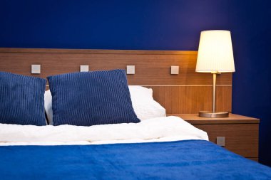 Mavi bir otel odasında, yatak ve lambanın ayrıntıları.
