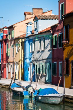 Burano adasında küçük renkli evlerle birlikte kanala park edilmiş tekneler.