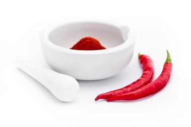 Beyaz havan topunun önünde, beyaz zemin üzerinde öğütülmüş kırmızı paprika baharatı olan beyaz topuz.