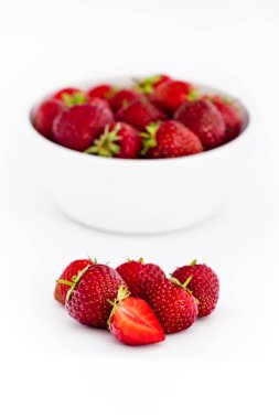 Çilek dolu beyaz kasenin önünde taze çilek yığını