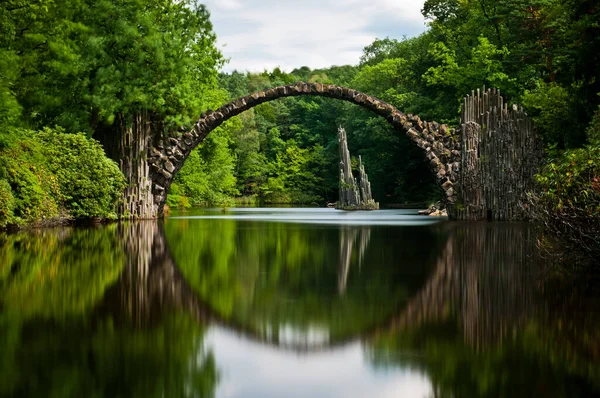 Very old stone bridge over the quiet lake with its reflection in the water, long exposure