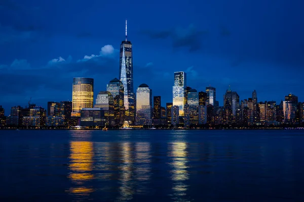 New York City Manhattan downtown skyline with skyscrapers illuminated over Hudson River panorama, including the One World Trade Center