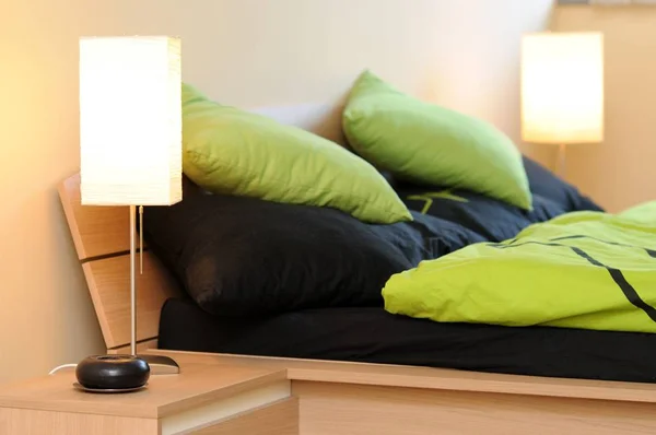Two lamps in a bedroom with green-black beddings