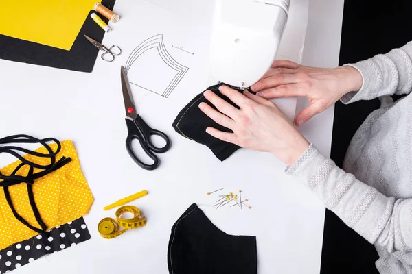 Kadın elleri koronavirüs pandemisi sırasında siyah yüz maskesi dikmek için dikiş makinesi kullanıyor. Tıbbi malzeme sıkıntısı nedeniyle yerli dikiş.