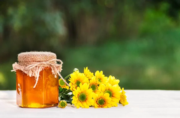 A jar of flower honey and yellow flowers. Fresh homemade honey