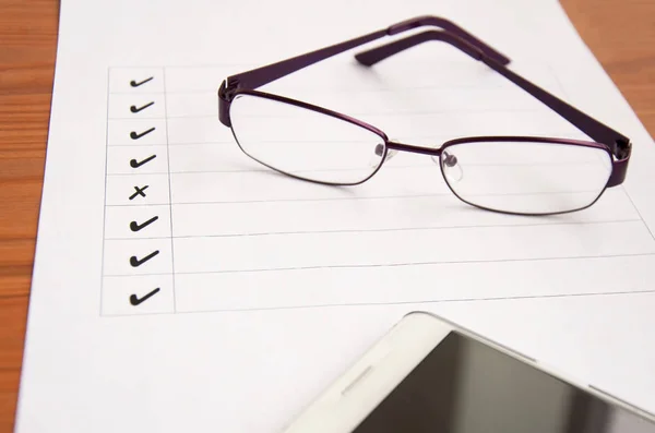 blank checklist on wooden table With coffee and glasses