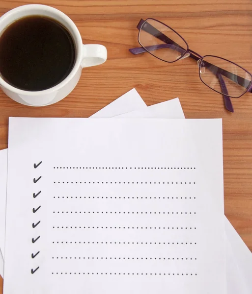 blank checklist on wooden table With coffee and glasses