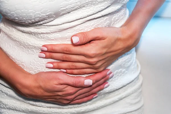 A young woman holds her hands on her stomach. The concept of IVF, pregnancy, digestion, the health of the female reproductive system. Menstrual pain. I have a stomachache.