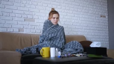 Kafkasyalı hasta genç kadınlar üşümüş ve titreyerek evlerinde sıcak gri ekoseli battaniyeyle titreyerek kanepede otururken grip virüsü gribi belirtileri gösteriyor.