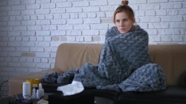 Kafkasyalı hasta genç kadınlar üşümüş ve titreyerek evlerinde sıcak gri ekoseli battaniyeyle titreyerek kanepede otururken grip virüsü gribi belirtileri gösteriyor.