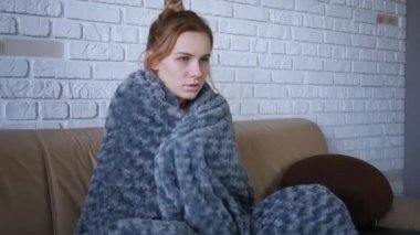 Kafkasyalı hasta genç kadınlar üşümüş ve titreyerek evlerinde sıcak gri ekoseli battaniyeyle titreyerek kanepede otururken grip virüsü gribi belirtileri gösteriyor.