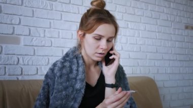 Evde grip olan ve vücut ısısını ölçen hasta bir kız. Akıllı telefon kullanıyormuş. Aile doktorunu ara.