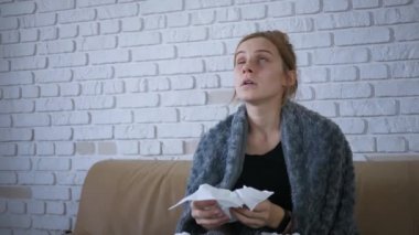 Genç bir kadının burun sümkürmesi, grip konsepti, mendile hapşırmış, kanepeye oturmuş, hasta bir kız, baca alerjisi belirtileri gösteriyor, peçeteyi evde tek başına tutuyor.