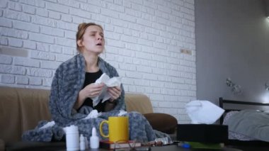 Genç bir kadının burun sümkürmesi, grip konsepti, mendile hapşırmış, kanepeye oturmuş, hasta bir kız, baca alerjisi belirtileri gösteriyor, peçeteyi evde tek başına tutuyor.