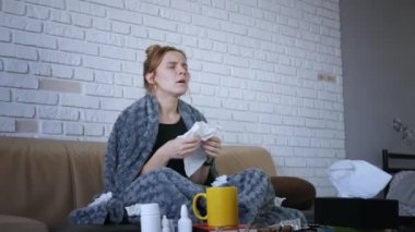 Genç bir kadının burun sümkürmesi, grip konsepti, mendile hapşırmış, kanepeye oturmuş, hasta bir kız, baca alerjisi belirtileri gösteriyor, peçeteyi evde tek başına tutuyor.