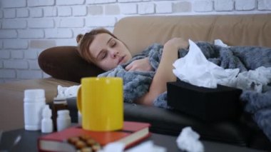 Genç bir kadının burun sümkürmesi, grip konsepti, mendile hapşırmış, kanepeye uzanmış, hasta bir kız, baca alerjisi belirtileri gösteriyor, peçeteyi evde tek başına tutuyor.