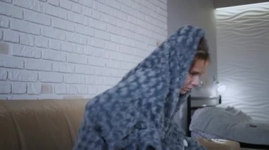 Güzel beyaz kadın hasta, kanepede oturuyor. Burnu tıkalı, hapşırıyor ve öksürüyor. Burnunu sümkür ve gri örtülerin altına saklan..