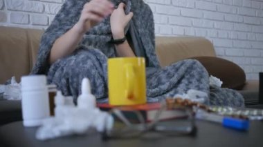 Güzel, beyaz, burnu akan bir kadın evde burun spreyi kullanıyor. Oturma odasındaki kanepede, battaniyenin altında oturuyor.