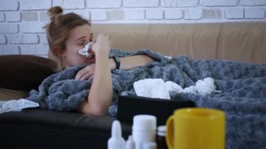 Güzel, beyaz, burnu akan bir kadın evde burun spreyi kullanıyor. Oturma odasındaki kanepede, battaniyenin altında yatıyor.