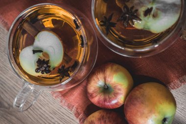 Elma şarabı, meyve suyu, meyve suyu, meyve suyu, baharatlı çay, tarçın çubukları, yıldız anason ve tahta zeminde taze elmalar. Sonbahar ve kış akşamları için sıcak içecek. Kapatın. Mevsimlik sıcak içecek..