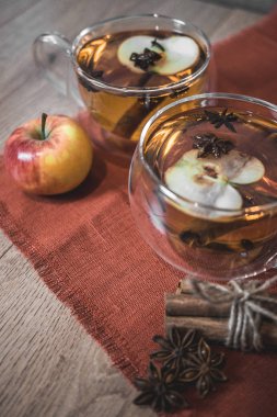 Elma şarabı, meyve suyu, meyve suyu, meyve suyu, baharatlı çay, tarçın çubukları, yıldız anason ve tahta zeminde taze elmalar. Sonbahar ve kış akşamları için sıcak içecek. Kapatın. Mevsimlik sıcak içecek..