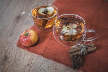 Elma şarabı, meyve suyu, meyve suyu, meyve suyu, baharatlı çay, tarçın çubukları, yıldız anason ve tahta zeminde taze elmalar. Sonbahar ve kış akşamları için sıcak içecek. Kapatın. Mevsimlik sıcak içecek..
