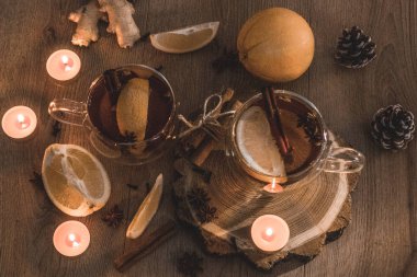 Tarçınlı portakal aromalı çay ve bardaklarda kakule, portakal ve tarçın çubuklarıyla ahşap bir masanın üzerinde mum ışığı. Ahşap arka planda sıcak şarap ve baharatlar. Seçici odaklanma. Kapat.. 