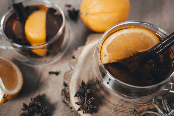 Апельсиновый чай с корицей и кардамоном в стаканах, оранжевые и коричные палочки на деревянном столе. Маллированное вино и специи на деревянном фоне. Выборочный фокус. Закрыть
. 