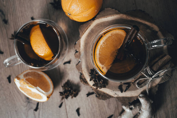 Orange flavored tea with cinnamon and cardamom in glasses, orange and cinnamon sticks on a wooden table. Mulled wine and spices on wooden background. Selective focus. Close up. 