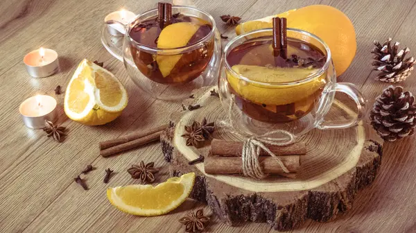 Orange flavored tea with cinnamon and cardamom in glasses, orange and cinnamon sticks lit by candlelight on a wooden table. Mulled wine and spices on wooden background. Selective focus. Close up.