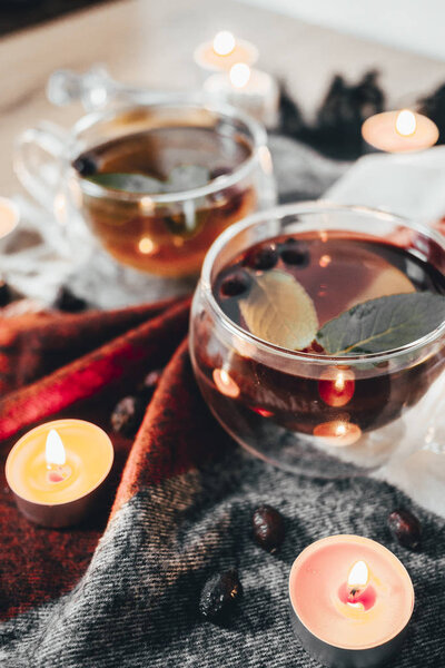 Black cup tea with dried rosehip and fresh leaves mint on the background of scattered dried rose hips and wax candles. Selective focus. Close up. Autumn and winter background. 
