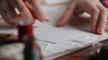 Genç terzi dokudaki desenleri aktarmak için kalem kullanır. Kadınların ellerini kapayın ve gece geç saatlerde kumaşa desenler çizin.. 