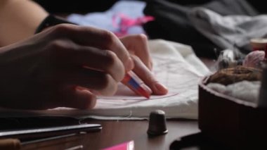 Genç terzi beyaz dokudaki desenleri aktarmak için kırmızı kalem kullanıyor. Akşam geç saatlerde kadınların elleri beyaz kumaşa desenler çiziyor.. 