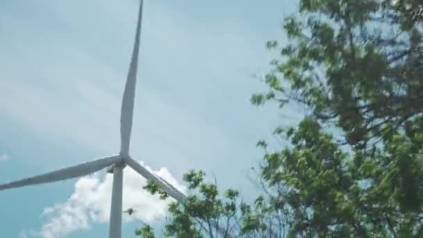 Een bewegende opname van een windturbine, het uitzicht is vanuit een bewegend voertuig met de auto. Heldere blauwe lucht met heldere witte wolken, opgenomen op een zomerse dag. Groene energie — Stockvideo