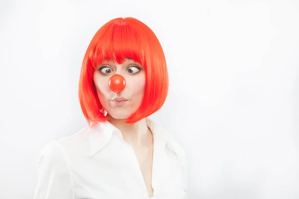 Bonita joven morena mujer caucásica con nariz roja y peluca haciendo una cara sobre fondo blanco — Foto de Stock